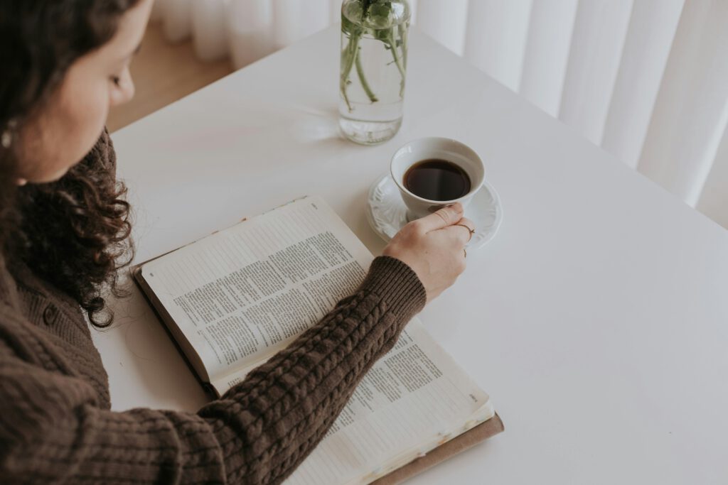 A woman enjoys a peaceful moment reading a book and sipping coffee at a bright indoor space.